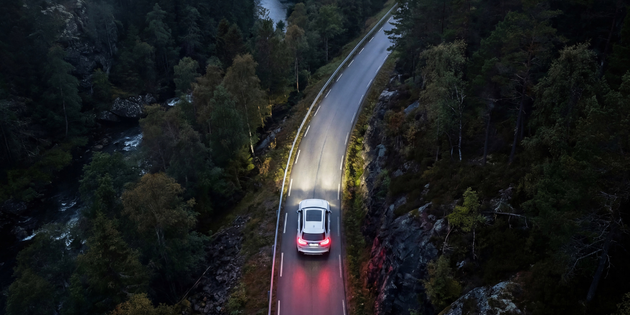 Aerial view of an electric car driving on a winding forest road at dusk
