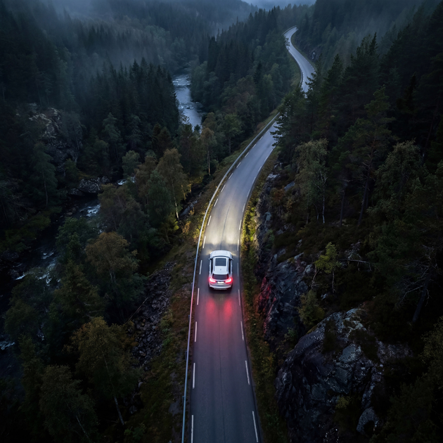 Aerial view of an electric car driving on a winding forest road at dusk