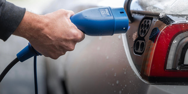 Wet hand connecting a blue Type 2 plug to the charging port of a red electric car